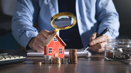 Real estate agent holding magnifying glass on house model.