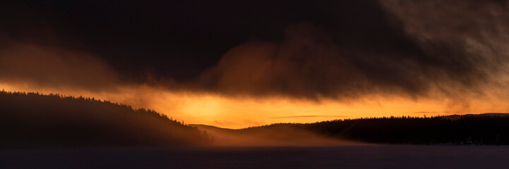 Dramatic stormy clouds at sunset over a forest and frozen lake in Lapland, inside teh Arctic Circle in winter, background with copy space