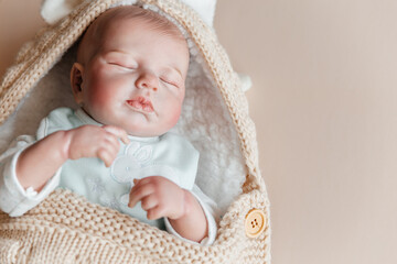 Reborn a boy doll sleeps in a knitted beige envelope. Copy space.