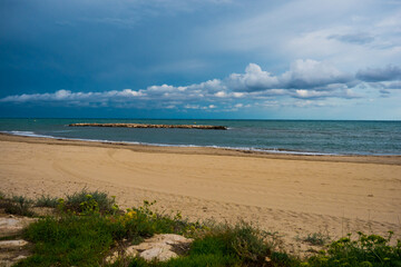 Seascape with sand shore, dark sky clouds, breakwater