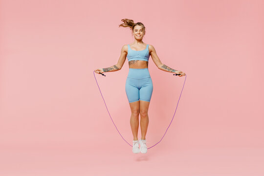 Full body young sporty athletic fitness trainer instructor woman wear blue tracksuit spend time in home gym using skipping rope isolated on pastel plain light pink background. Workout sport concept.