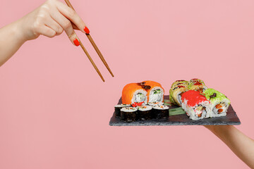 Close up cropped female hold chopsticks makizushi sushi roll served on black plate traditional japanese food isolated on pastel plain light blue color wall background. Copy space advertising mock up.