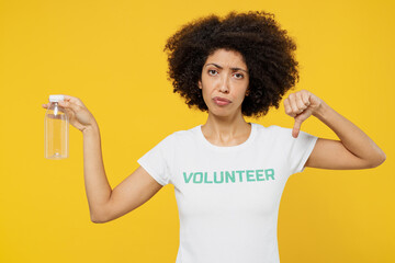 Young woman of African American ethnicity in white volunteer t-shirt hold plastic bottle show thumb down isolated on plain yellow background. Voluntary free work assistance help charity grace concept.