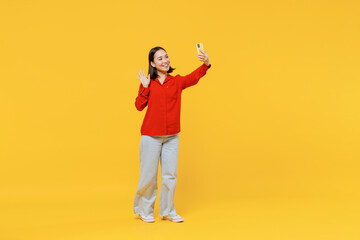 Fototapeta na wymiar Full size body length fun young woman of Asian ethnicity 20s in casual clothes doing selfie shot on mobile cell phone post photo on social network isolated on plain yellow background studio portrait.