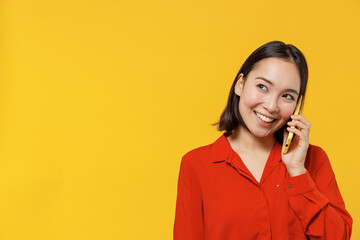 Happy young woman of Asian ethnicity 20s years old wears orange shirt look aside talk speak on...