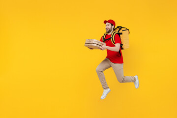 Fototapeta na wymiar Side view full size delivery guy employee man in red cap T-shirt uniform work as dealer courier jump high hold cardboard box run fast jump thermal food bag backpack isolated on plain yellow background