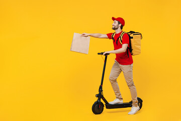 Full body delivery employee man in red cap T-shirt uniform work as dealer courier ride kick scooter hold thermal food backpack brown blank craft paper takeaway bag isolated on plain yellow background.