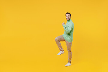 Fototapeta na wymiar Full body smiling happy young man 20s wear mint knitted sweater doing winner gesture celebrate clenching fists say yes isolated on plain yellow background studio portrait. People lifestyle concept.