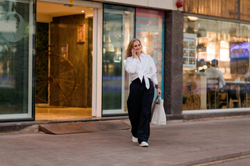 A young woman on the street with shopping bags talking on a mobile phone