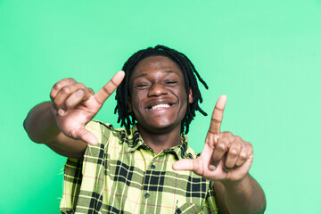 Naklejka premium Young black man with dreadlocks smiling and making frame gesture