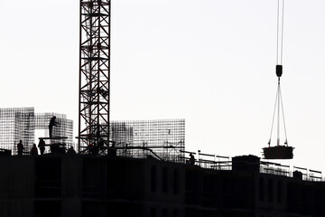 Silhouettes of workers and tower crane on construction site against the sky. Housing construction, builders working on scaffolding - obrazy, fototapety, plakaty
