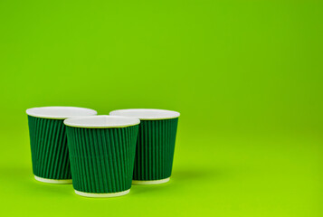 Disposable paper cups on a green background. Ecological coffee utensils. Copy space and free space for text near the glasses.