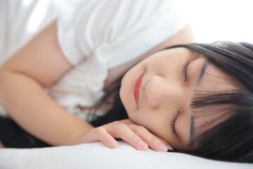 Beautiful young Asian woman sleeping on bed relaxing in the morning light with white room