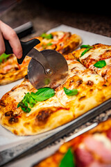 chef hand with cutter cutting pizza to pieces at pizzeria