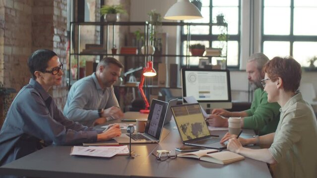 Tilt down shot of two female colleagues smiling and having discussion while working at coworking table in modern open space office