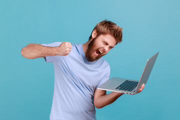 Portrait of man punching laptop screen, looking with furious mad expression, boxing threatening to...