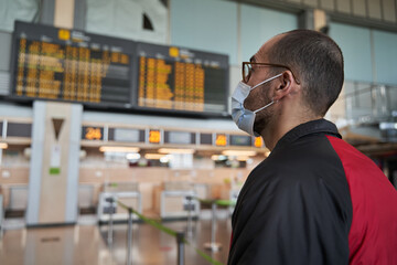 Airport during covid-19 pandemic concept. Delays and cancelation. Man with face mask in empty...