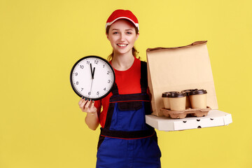 Portrait of smiling courier woman holding wall clock and coffee with pizza box, express delivery in...
