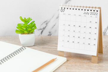 July 2022 desk calendar with plant on wooden table.