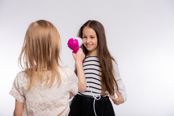 Two beautiful girls 6-8 years old are playing with the hair dryer. Girls playful spending time together and drying hair over white background