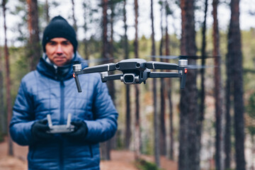 Man Operating Drone Flying or Hovering by Remote Control in fall forest.