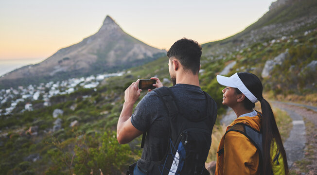This view is simply stunning. Shot of a young couple taking photos while out on a hike in a mountain range outside.
