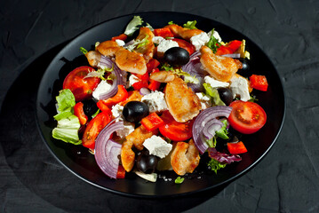 Salad with tomatoes, peppers, olives and chicken fillet. Fresh salad in a black plate on a dark background.