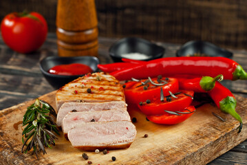 Steak with sliced tomatoes on a cutting board. Meat on a dark wooden background. Food, sauce, salt, pepper and spices on an old shabby table.