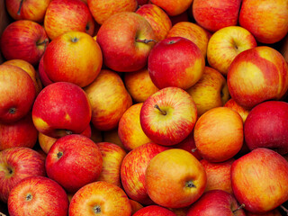Lots of red and yellow apples in a box. Texture of round apples close up. Sale of fruit at the market and supermarket.