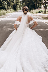 Fototapeta na wymiar The bride in a long veil runs along the road. Photo from the back