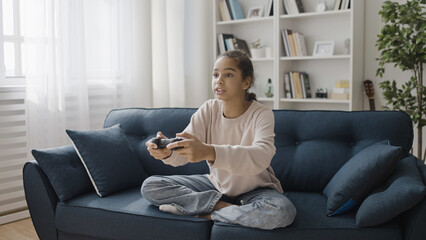 Obraz premium Teen girl playing video game at home, pressing buttons on joystick, modern technology