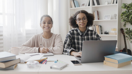 Two teen girls smiling at camera, learning foreign language at home, internet