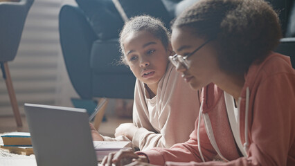 Two African American teen girls studying on floor, doing homework together