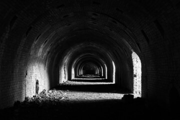 Obraz premium A dark dilapidated tunnel with sunlight falling in in black and white