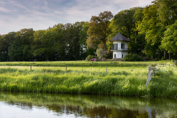 A small white tower in the middle of a meadow along a ditch in the Netherlands