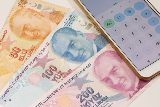 50, 100 and 200 Turkish lira banknotes with Ataturk's picture on it and calculator app open mobile phone on isolated background. Time is money concept.