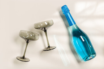 Blue champagne or sparkling wine bottle, champagne glasses from tinted gray glass on beige...