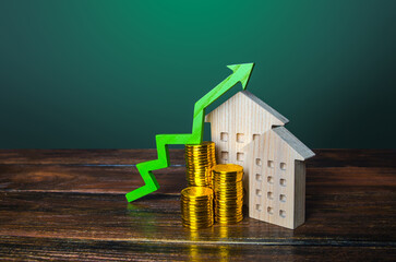 Green arrow up over wooden houses. Increasing cost of housing concept. High demand for real estate....