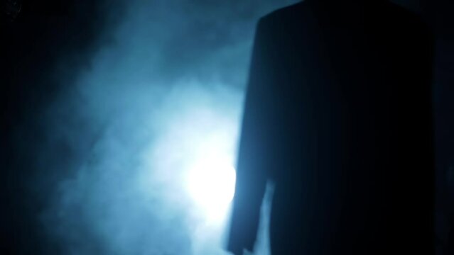 Cinematic slow motion shot of a gangster mafia man walking with a gun in his hand. Dramatic shot of a man in dark lighting with some smoke clouds around him. High-resolution footage.
