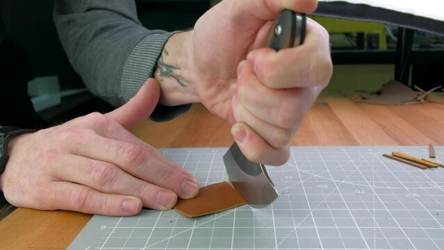 Close up hands tanner cuts special halberd cutting knife leather piece in workshop. Craft production.