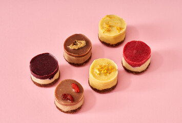 Colorful healthy raw vegan no-bake mini cheesecakes on pink background
