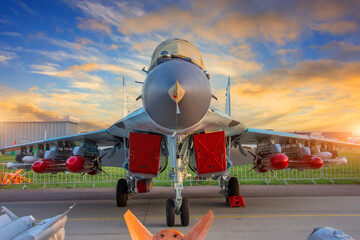 Fighter with covered engines and live ammunition on the wings in the parking lot during sunset.