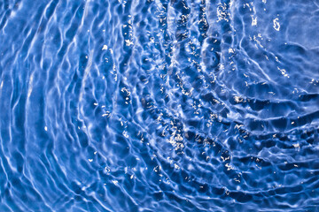 Waves of water in sunlight. Blue transparent texture of the water surface with splashes and waves....