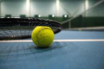 Close-up of yellow tenis ball under racket on blue hard tenis court.