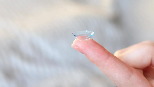 Women's finger with contact lens on a blurred background