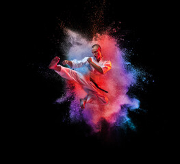 Collage. Young sportive man in white kimono practising, training martial arts, karate isolated over black background with colorful powder explosion