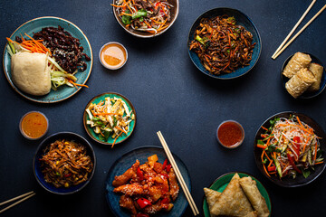 Set of Chinese dishes on table: sweet and sour chicken, fried spring rolls, noodles, rice, steamed buns with bbq glazed pork, Asian style banquet or buffet, top view with copy space
