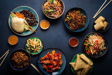 Set of Chinese dishes on table: sweet and sour chicken, fried spring rolls, noodles, rice, steamed buns with bbq glazed pork, Asian style banquet or buffet, top view with copy space
