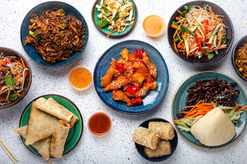 Set of Chinese dishes on white table: sweet and sour chicken, fried spring rolls, noodles, rice, steamed buns with bbq glazed pork, Asian style banquet or buffet, top view copy space
