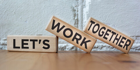 Let's work together words on wooden blocks, against the background of a white brick wall